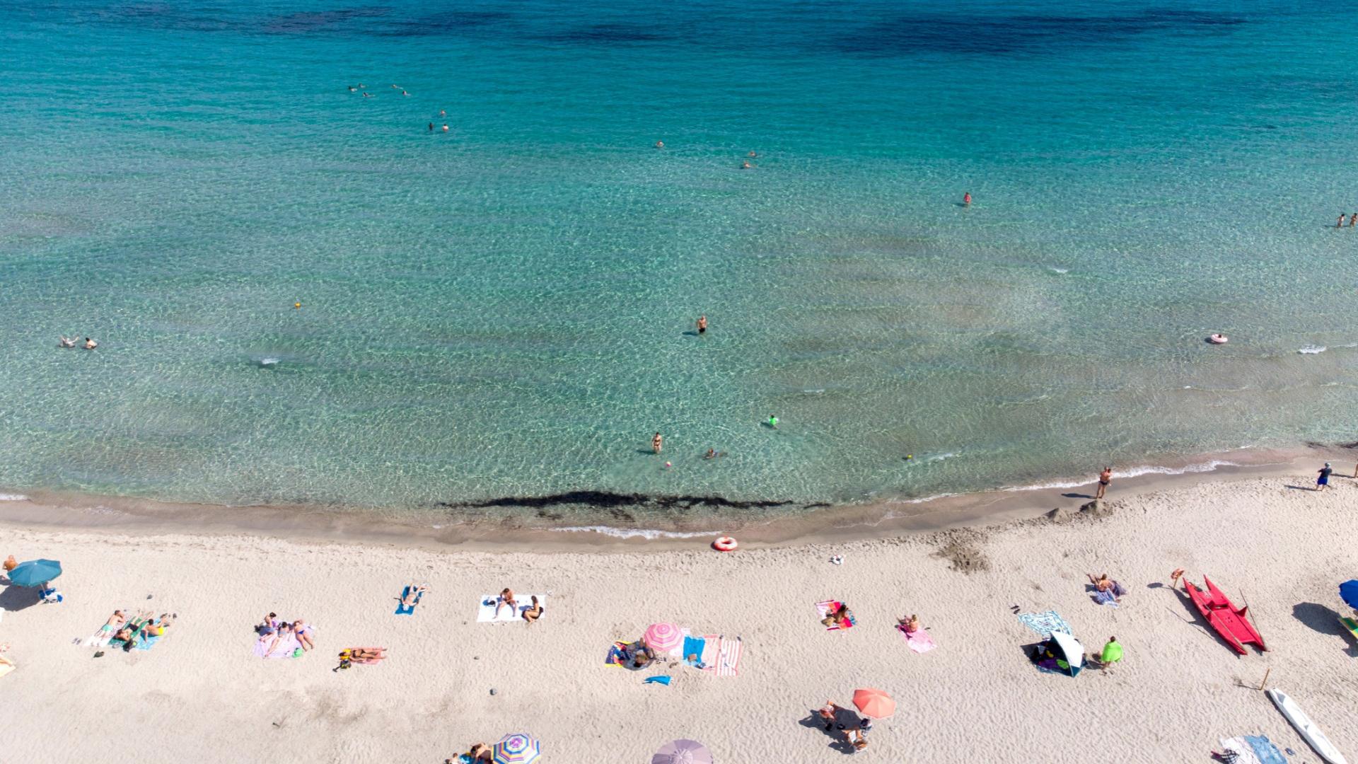Spiaggia con mare cristallino, ombrelloni colorati e bagnanti che si rilassano al sole.